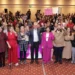 Celebración y apoyo en evento de mujeres, con oradores y participantes uniendo fuerzas.