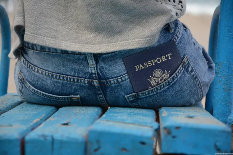 1. Pasaporte en el bolsillo trasero de jeans en banco de madera azul.