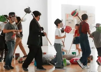 Esquina de niños y adultos participando en obra de teatro escolar con accesorios creativos.