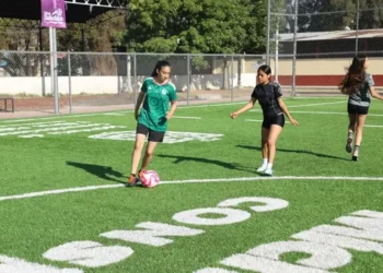 Balón de fútbol y niñas jugando en campo de césped artificial.