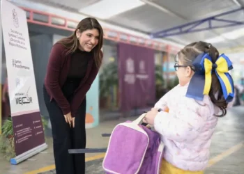 Sujeto interactuando con una niña en un evento escolar en un espacio cubierto.