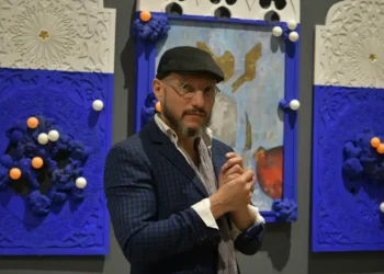 El hombre en la galería de arte con fondo azul y obras decorativas.