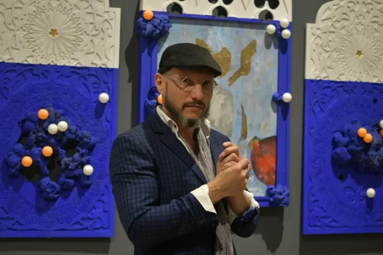 El hombre en la galería de arte con fondo azul y obras decorativas.